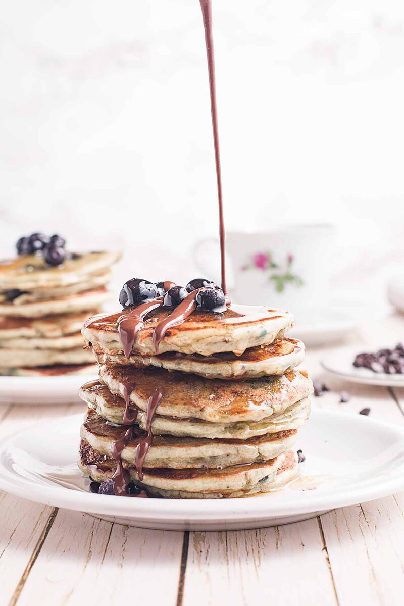 Stack of pancakes with chocolate syrup poured on top, bright background